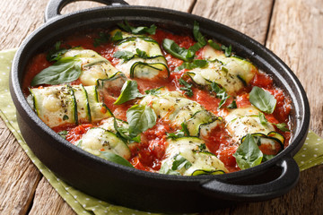 Baked zucchini rolls with ricotta cheese and herbs in tomato sauce in a pan close-up. horizontal