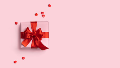 Pink gift box with red bow on pink background with red hearts around. Holiday web banner. Top view....