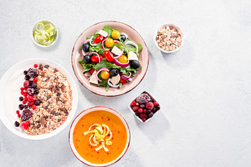 Carrot cream soup, Greek salad, granola bowl with yogurt on concrete table top with copy space. Assortment of dishes for diet, suitable for volumetrics diet and other nutrition strategies, top view