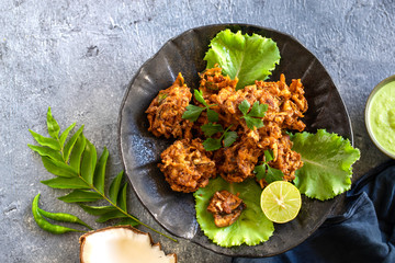 Indian cuisine. pakora traditional Indian deep-fried snack. pakoras on black plate with coconut chutney sauce curry leaves. national appetiser authentic vegetarian food. Asian travel food. top view.