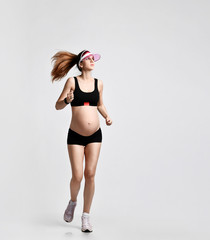 Pregnant girl in green sun visor, black sport shorts and top, pink sneakers. She is jogging isolated on white. Full-length