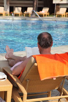 リゾートホテルのプールサイドで読書をする男性のイメージ
