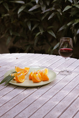 Red wine served outside in garden on white table with fresh orange in sun lights close up