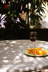 Red wine served outside in garden on white table with fresh orange in sun lights close up
