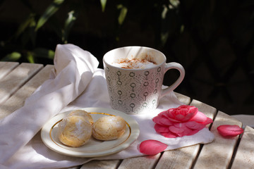 White porcelain cup of hot coffee, cappuccino with three Italian amaretti cookies.Summer breakfast in a terrace - coffee, amaretti and flowers