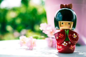 Wooden Japanese Kokeshi Doll dressed in traditional kimono, hand painted in red and florals. Pink cherry blossom background