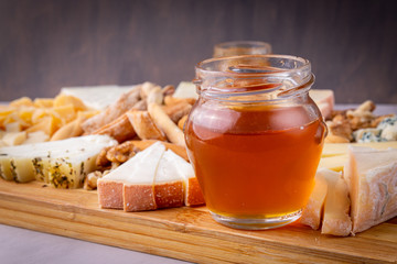 Close-up of a jar of honey accompanied by various kinds of cheese