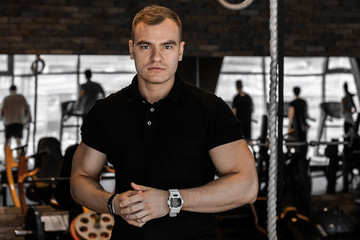Fototapeta na wymiar Portrait of young masculine fitness trainer man in gym while training around fitness equipment looking into the camera.