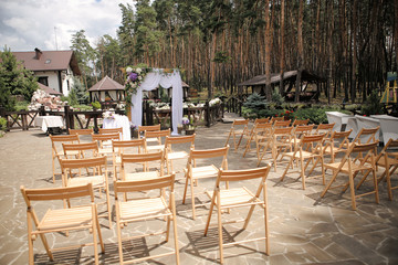 Wedding decoration. Arch with white textile curtain and purple flower decor. Wooden elements. Outdoor wedding ceremony in the coniferous forest. Selective focus