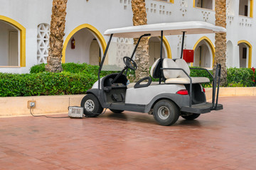 A white Golf cart is parked near the hotel complex. The electric car is charged in the Parking lot...