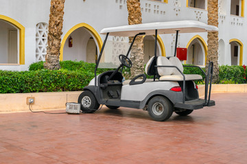 A white Golf cart is parked near the hotel complex. The electric car is charged in the Parking lot of the resort city. A car standing alone. © Климов Максим