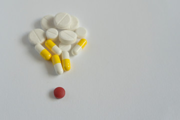 one red pill with many white and yellow  pills on white background. copy space