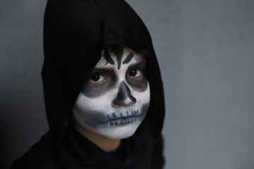 niño con disfraz de muerte con la cara pintada como una calavera yla capucha negra puesta