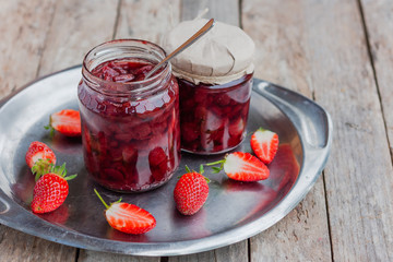 Strawberry jam in a glass jar with some fresh strawberry on steel vintage plate on wooden old rustic table. Homemade strawberry marmelade and fruits. Selective focus.