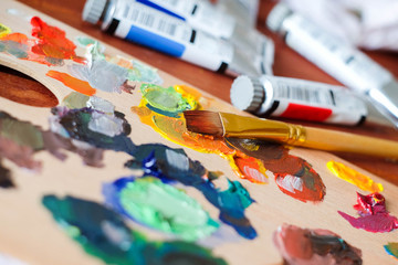 Fototapeta premium Close up oil painting process. Oil paints palette. Oil painting tools on the wooden table. Painter work place. Paint tubes and paintbrush. Mixing paints.