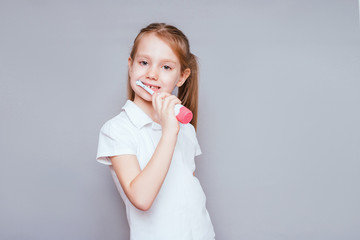 little cute girl smiles and brushes her teeth with a colored brush on a gray background. dental hygiene. happy little girl brushes her teeth