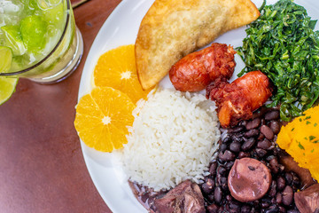 brazilian feijoada on white plate. Accompanied by rice, sausage, cabbage, pastry and caipirinha