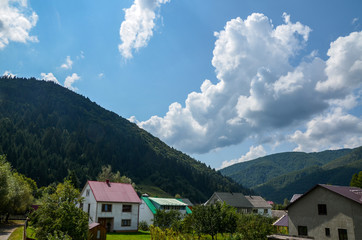 Fototapeta na wymiar View on Carpathian village Kolochava, Houses and coniferous foreston hills on background. Beautiful summer landscape, cloudy sky at bright sunny day. Travel background.