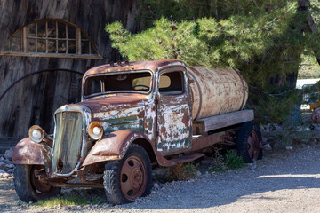 Vintage tanker truck rusting in the desert beside an old barn