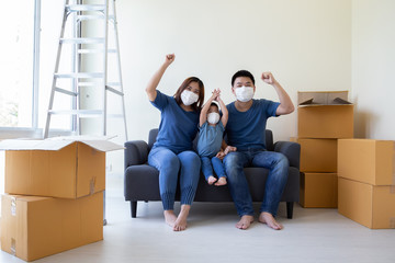 Fototapeta na wymiar Asian family wearing protective medical mask for prevent virus covid-19 and hand up during moving day and relocating at new home. Moving house and new real estate concept