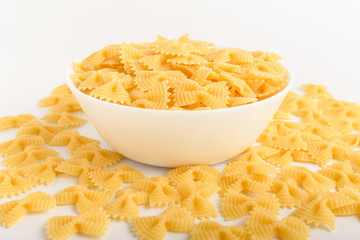 Dried Farfalle Rigate traditional Italian pasta on a plate ready to be cooked, isolated on a white table, side viewof healthy food 
