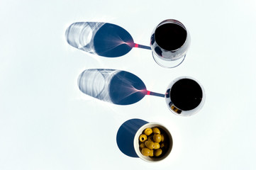 Two glasses of red wine and olives on white with hard light.