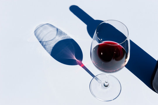 Glass and bottle of red wine on white with hard light.