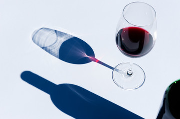 Glass and bottle of red wine on white with hard light.