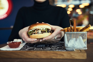 Hands holding fresh delicious burgers with french fries, sauce and beer on the wooden table top view. - 341419596