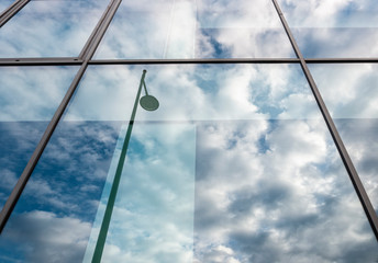 Cloud reflections and street lamp in a window of a facade