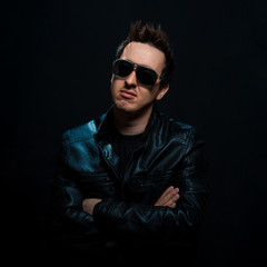 Obraz premium Young sexy stylish guy with glasses in a black leather jacket on a black background