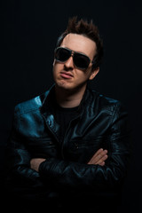 Obraz premium Young sexy stylish guy with glasses in a black leather jacket on a black background