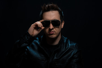 Young sexy stylish guy with glasses in a black leather jacket on a black background