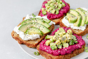 Variation of healthy sandwiches with avocado beetroot cream cheese and whole wheat rye bread on a plate on grey background.   Delicious snacks and toast. Food composition. Close up, top view