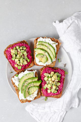 Variation of healthy sandwiches with avocado beetroot cream cheese and whole wheat rye bread on a plate on grey background. Delicious snacks and toast. Food composition. Top view