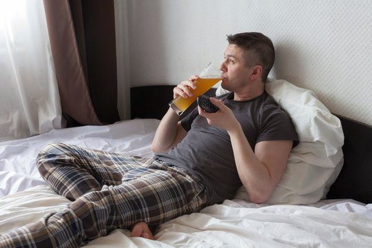 man in bed with beer watching TV. Alcoholism from boredom during Covid-19 coronavirus quarantine epidemic. Stay at home concept.