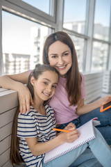 Cheerful mom and daughter sitting hugging on the floor.