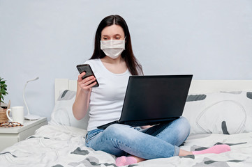 Work Home or Distance Online Learning on Quarantune. Woman in Protective Face Mask Remotely Working on Bed Using Laptop and Talking on Phone