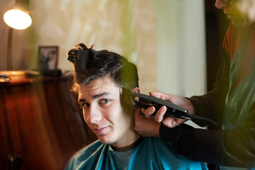 A woman cuts her hair to her teenage son, a guy smiles because he likes to be neat and have a nice...