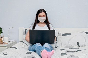 Work Home or Distance Online Learning on Quarantune. Woman in Protective Face Mask Remotely Working on Bed Using Laptop