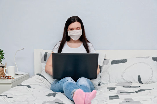 Work Home or Distance Online Learning on Quarantune. Woman in Protective Face Mask Remotely Working on Bed Using Laptop