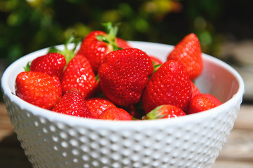 Strawberry berries in a white bowl on a wooden background.