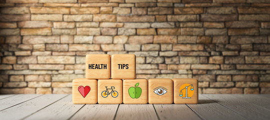 Fototapeta na wymiar cubes with text HEALTH TIPS and health icons in front of a brick wall on a wooden floor