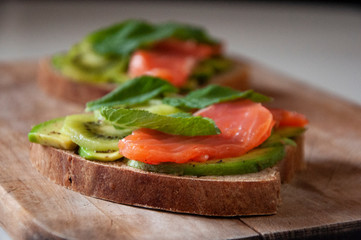 Healthy sandwich for breakfast made with home baked bread, salted salmon, avocado, kiwi and mint leaves.