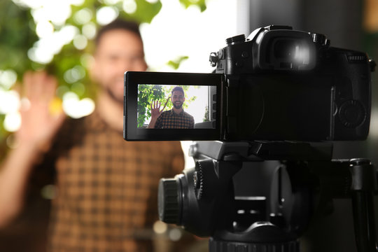 Young blogger recording video indoors, focus on camera screen