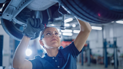 Portrait Shot of a Female Mechanic Working Under Vehicle in a Car Service. Empowering Woman Wearing...