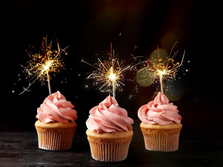 Birthday cupcakes with sparklers on table against dark background
