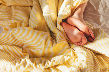 The feet of a sleeping man in the striped yellow bed linen. Sunny bedroom. Good morning