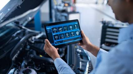 Car Service Manager or Mechanic Uses a Tablet Computer with a Futuristic Interactive Diagnostics Software. Specialist Inspecting the Vehicle in Order to Find Broken Components In the Engine Bay. © Gorodenkoff