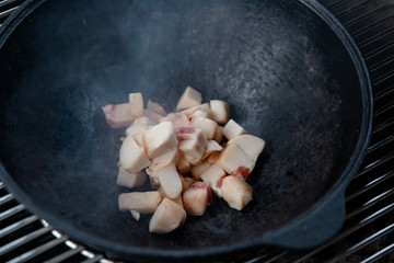 Pieces of lamb with onion are fried in boiling oil on the fire. As a stage in the preparation of traditional pilaf.step-by-step process of cooking pilaf in a cast iron cauldron on grill.
